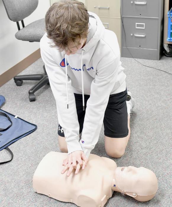 With two hands centered on the manikin’s chest, Logan Schroedl demonstrates how to give chest compressions during CPR.