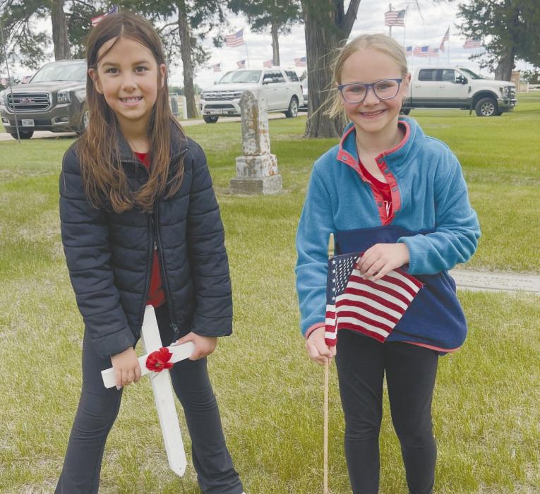 Brynn Pierce (left) and Gracyn Peterson (right) helped place flags and crosses to prepare for the Memorial Day service.