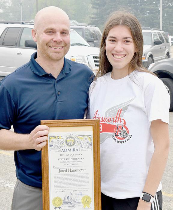 Jared Hansmeyer is retiring from teaching at Ainsworth High School and retiring as the Activities Director and Cross Country Coach. To honor Hansmeyer, the 2022-23 Cross Country Team contacted the State of Nebraska and asked that Hansmeyer be made an Admiral in The Great Navy of the State of Nebraska which Govenor Pillen granted. Katherine Kerrigan (right) presented Hansmeyer (left) with this Admiralty plaque at the State Track Sendoff on Thursday, May 18th.