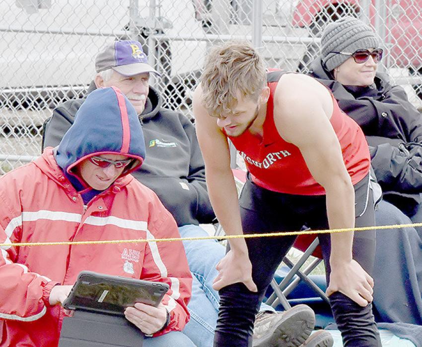 With spectators bundled up against the cold wind, Ainsworth Jumping Coach Wade Alberts and Owen Blumenstock review his jumps. Blumenstock took first place in the Boys Long Jump with a jump of 20’ 2.25” and fourth in the Boys Triple Jump with 38’ 5.5”.