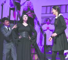Gomez Addams, played by Colby Beegle, hides from Wednesday Addams, played by Raelynn Reagan (far right). He hides behind Morticia Addams, who is played by Madison Phares.