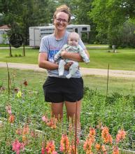Melissa Stewart stands behind her bed of snap dragons with her youngest son, Bridger (3 months).