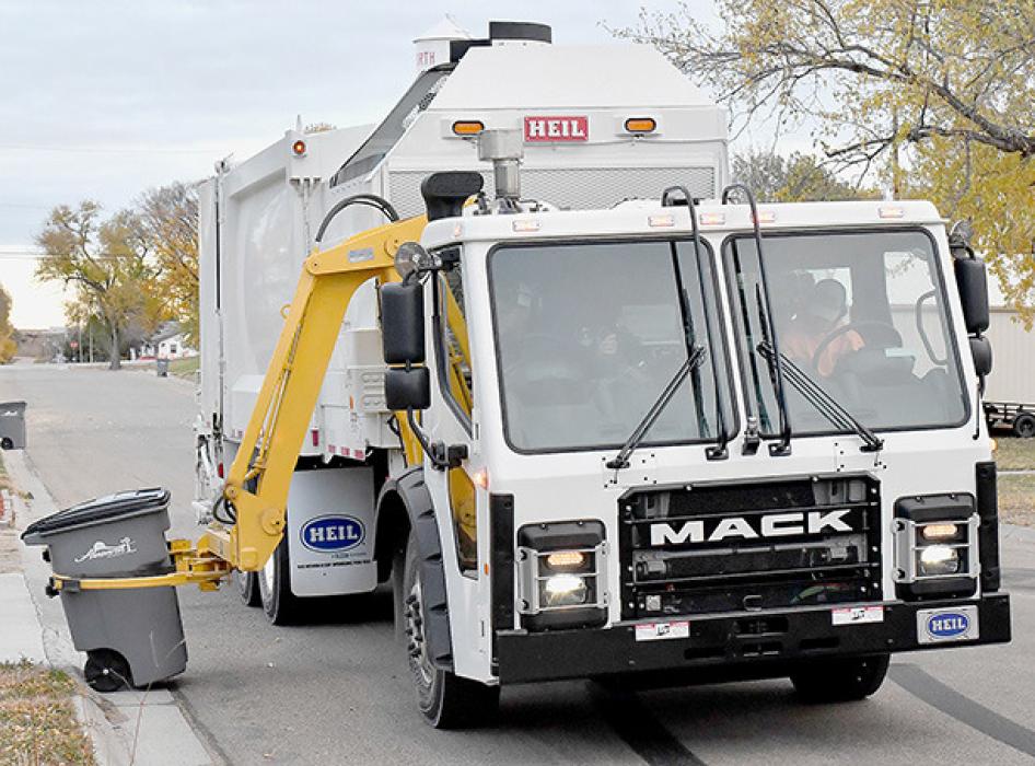 The new garbage truck pulls up beside totes that are placed curb side and clamps around the tote.