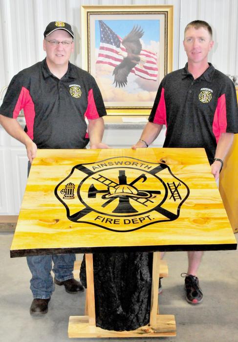 Ainsworth Fire Chief Brad Fiala (left) accepted this beautiful table made and designed by Ainsworth Firemen Lee Conroy (right). The table was made out of the tree that was struck by lighting that started the 2012 Niobrara River Valley Wildfires. The table is kept at the Fire Hall as a remembrance of the day that the whistle sounded and the aftermath that followed.