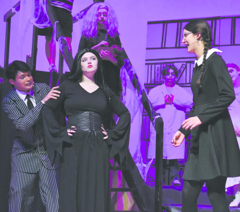 Gomez Addams, played by Colby Beegle, hides from Wednesday Addams, played by Raelynn Reagan (far right). He hides behind Morticia Addams, who is played by Madison Phares.