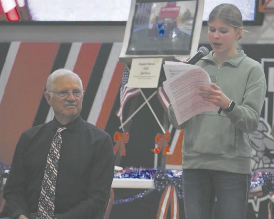 Eighth-grader Miranda Lambrecht reads her portion of the class’ adopted veteran speech. This year’s adopted veteran, Joel Ferris, sits beside her.