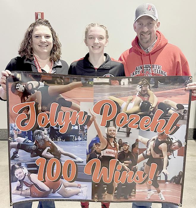 With her Quarterfinal win over Ella Reeves of Battle Creek, Jolyn Pozehl recorded her 100th High School Wrestling Victory. Her parents, Jessica (left) and Matt (right) were ready for the momentous win with a special banner.