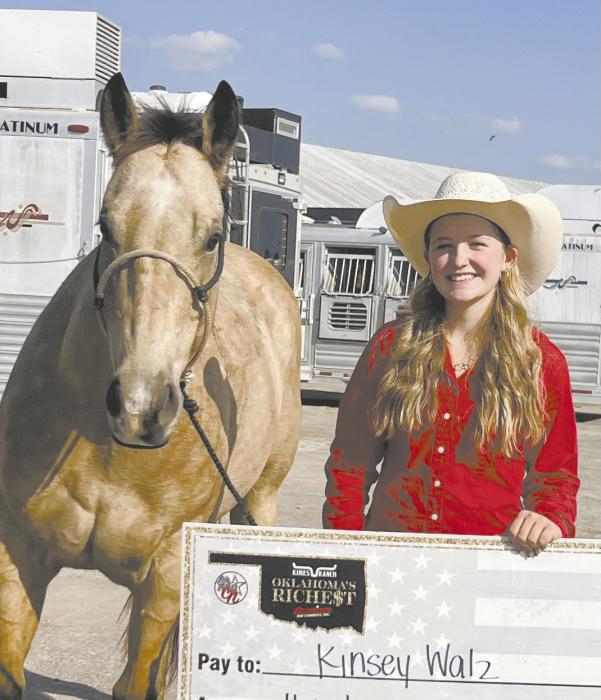 Kinsey Walz stands with her horse and holds her reward check for winning the 19 and under pole bending competition.
