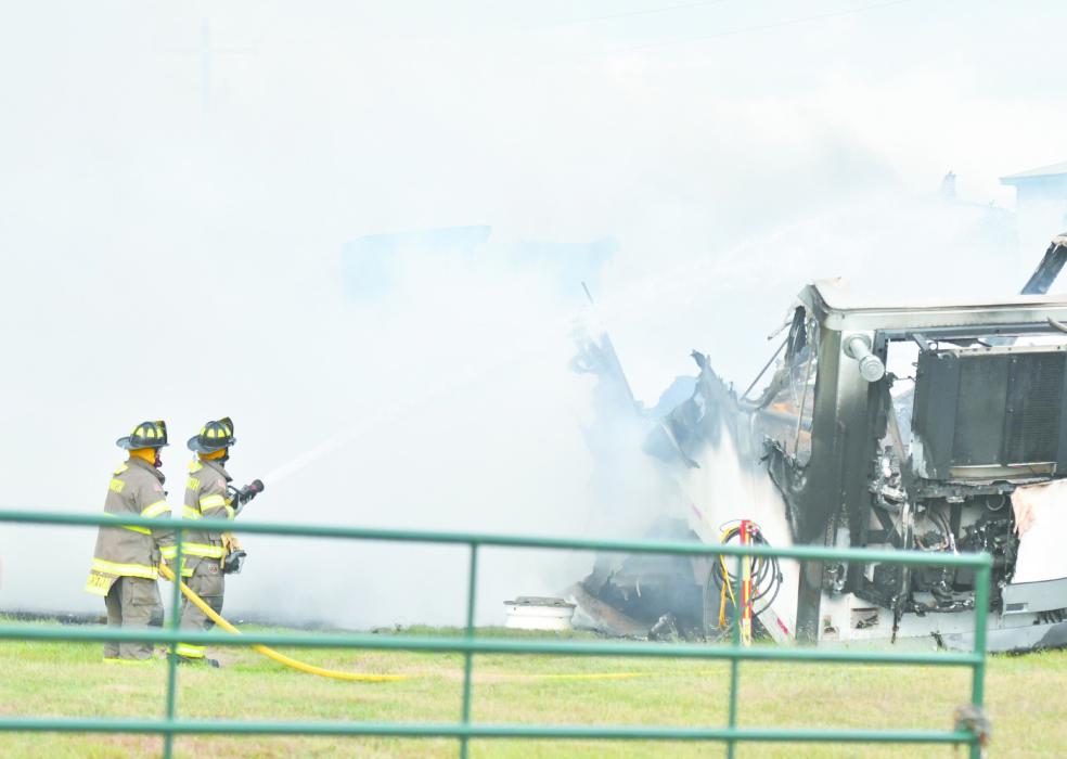 Two Ainsworth firemen use a hose to put out the feed trailer fire, caused by an apparent propane leak, on Thursday.