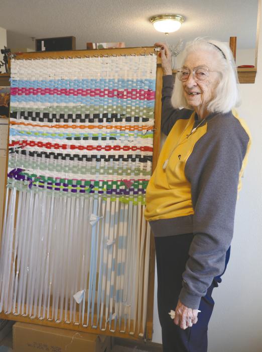 Lila Heerten stands with the mat she is currently weaving on the loom her son crafted for her.