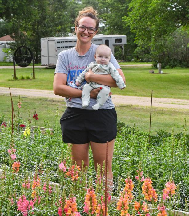 Melissa Stewart stands behind her bed of snap dragons with her youngest son, Bridger (3 months).