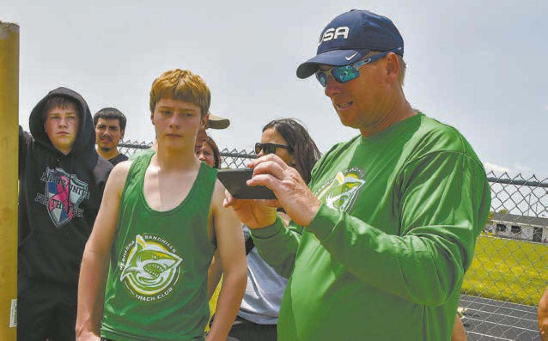 Shark’s head coach Wade Alberts reviews film and offers long jumper Cohen Keller (Bassett) critiques during the competition in Cozad.