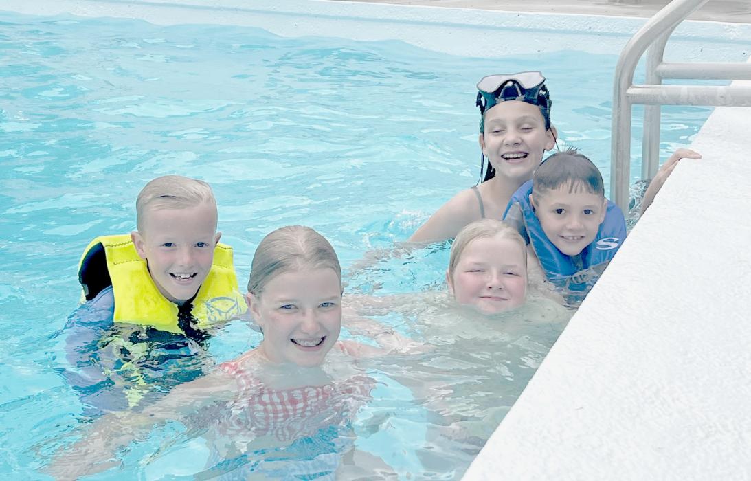 Sunscreen, swim gear, and splashing galore! Five children give big grins as they enjoy a dip in the pool during summer vacation.