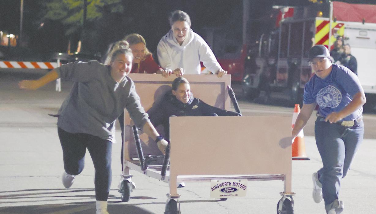 The bed race team of Karissa Beck, Jocelyn Good, Karli Kral, and Gracie Kinney push the bed down Third St. as April Good rides atop the bed. The team placed last after some troubles shucking a corn cob during the team’s challenge.