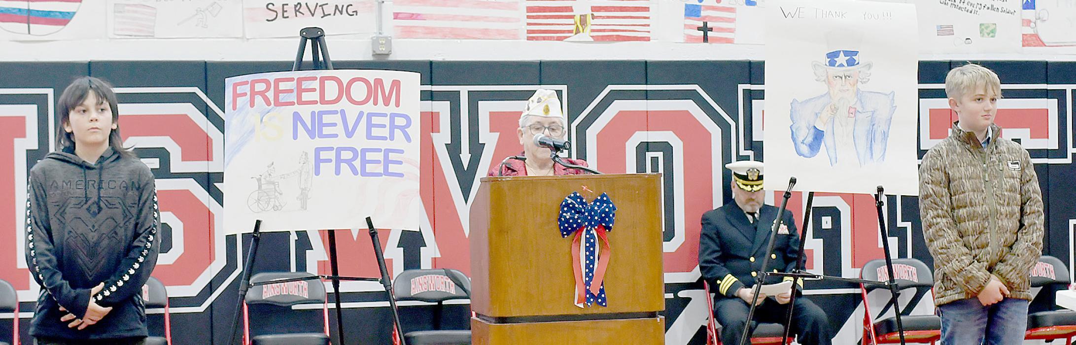 American Legion Commander of District 1, Judy Walters (center) introduced the local veterans. The two boys, Kolby Swett(Left) and Teigen Marbry (right) stand beside the Veteran posters they drew. The posters have been selected to be sent to Kearney for display in the Veteran’s Home.