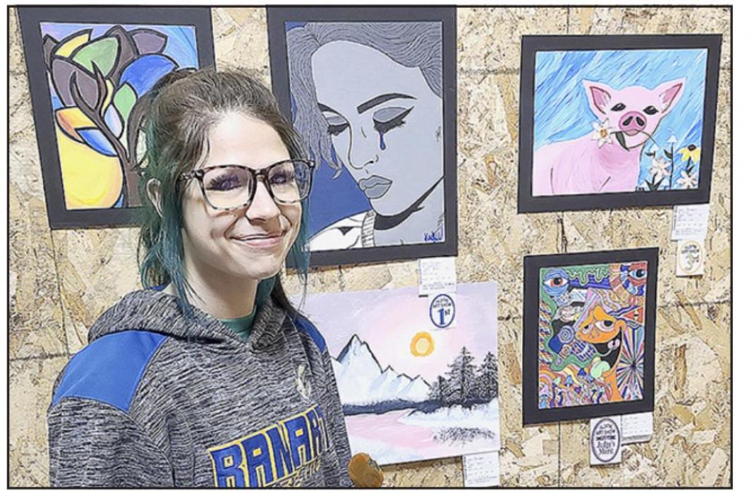 AHS junior Kaitlynn Inbody stands next to two of her art pieces. The grey-faced woman with a lone tear is named Ophelia and was done in acrylic. It took first place. On the lower right is her second acrylic piece, which is extremely colorful and has the words “Good Bye” in the upper right corner. This painting received the Judge’s Merit.