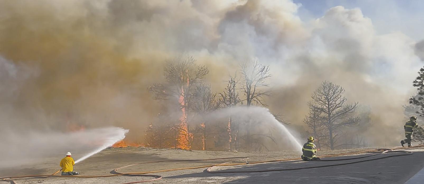 As the fire creeps up on a structure, firemen use water as a line of defense. The fire resulted in the loss of 45 head of cattle, along with the burning of a cabin and over five power poles. Multiple firefighters from various departments worked dilligently to protect as many houses and other structures as possible. Photo Courtesy of Ann Fiala